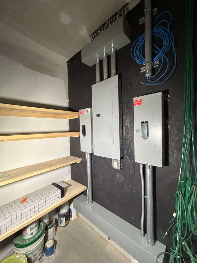 Electrical panel installation with conduits and storage shelves in a work area.