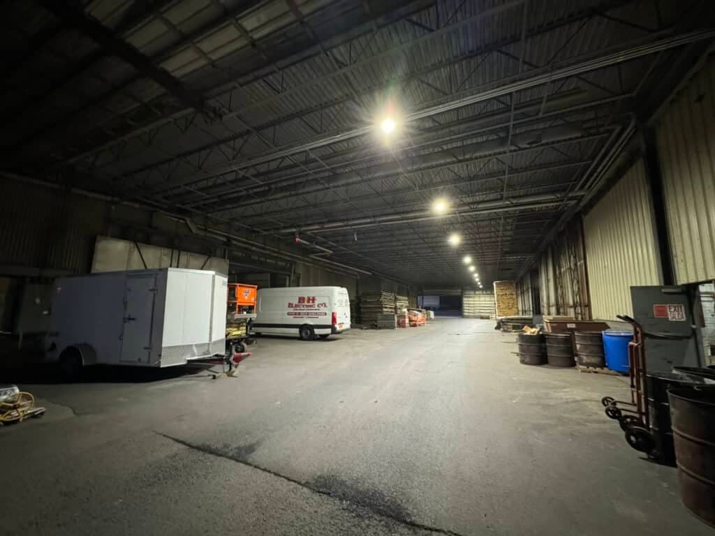 Interior of a large warehouse with lighting, vehicles, and storage barrels.