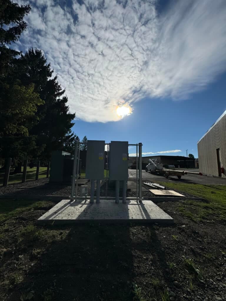 Electric utility infrastructure under a bright sky with clouds and trees in the background.