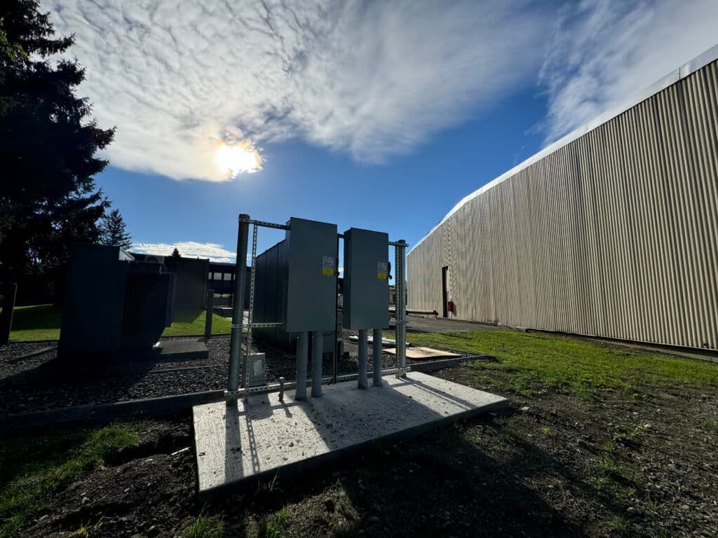 Electrical utility equipment with cloudy sky and building in the background.