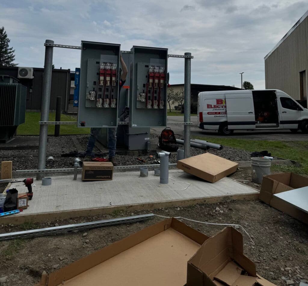 Electrician installing power distribution panels outside commercial building with tools and equipment.