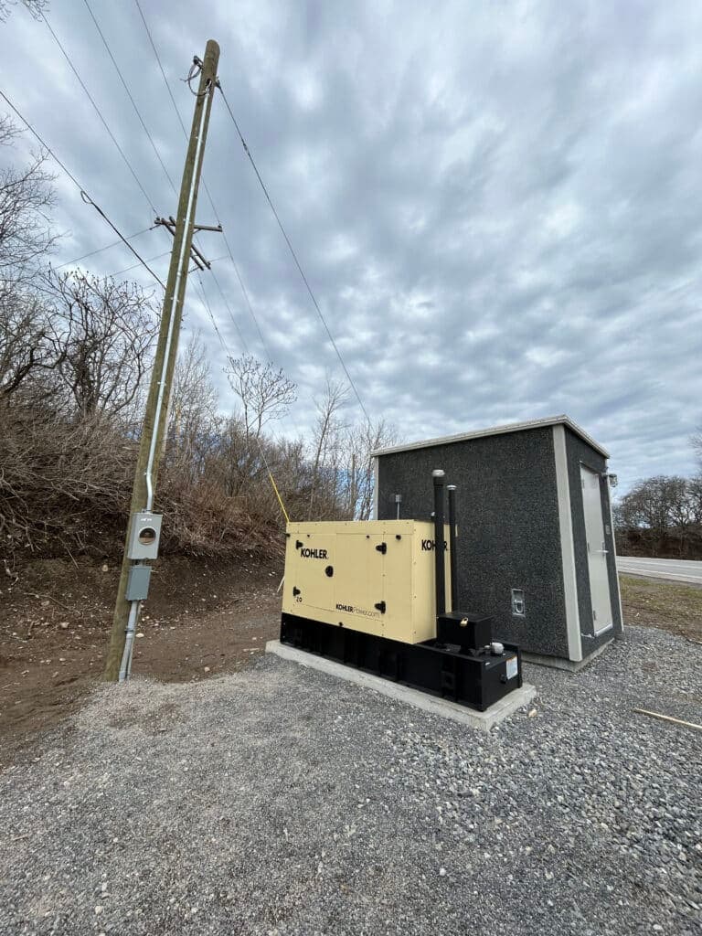 Kohler generator installation next to utility pole and power shed under cloudy sky.
