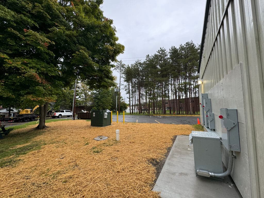 View of a commercial building’s side with utility equipment and landscaped area.