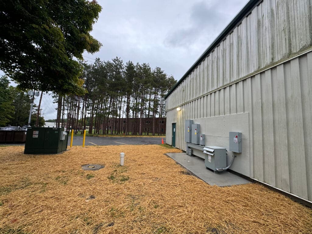 Utility area with electrical boxes and green transformer against a tree line and cloudy sky.