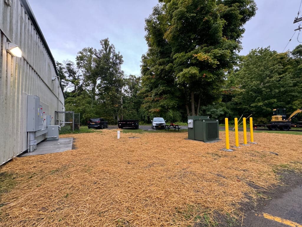 Outdoor utility area with equipment, vehicles, and trees, featuring straw ground cover.