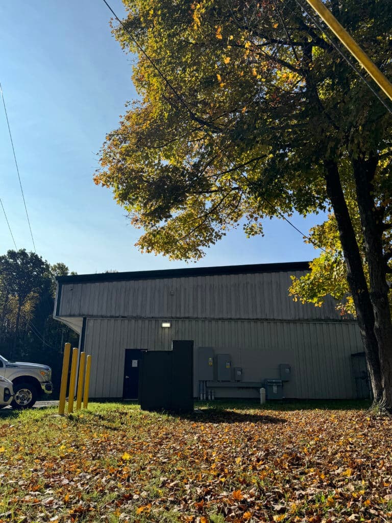 Metal building with trees and autumn leaves, surrounded by power lines and equipment.