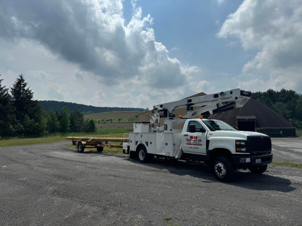 Utility truck with aerial lift parked on rural gravel lot under partly cloudy sky.