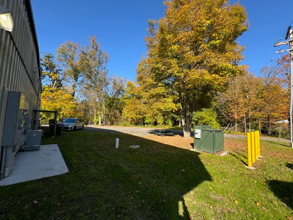 Industrial area with autumn trees, power box, and paved road under clear blue sky.