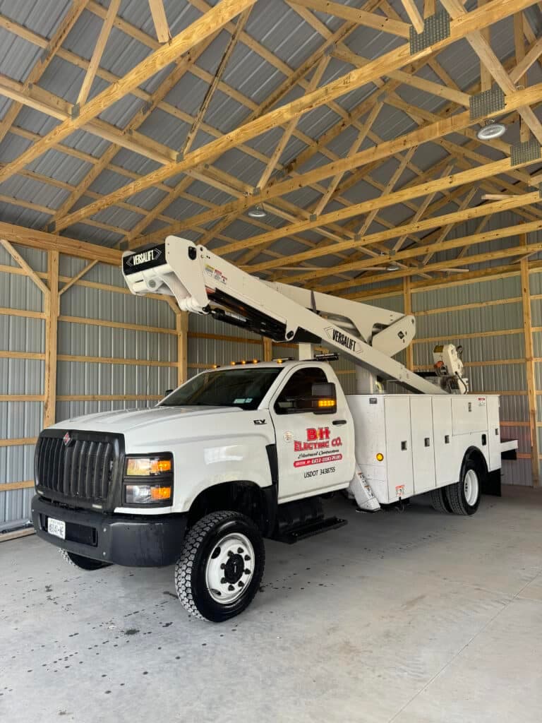 Bucket truck from B&H Electric Co parked in a spacious wooden garage.